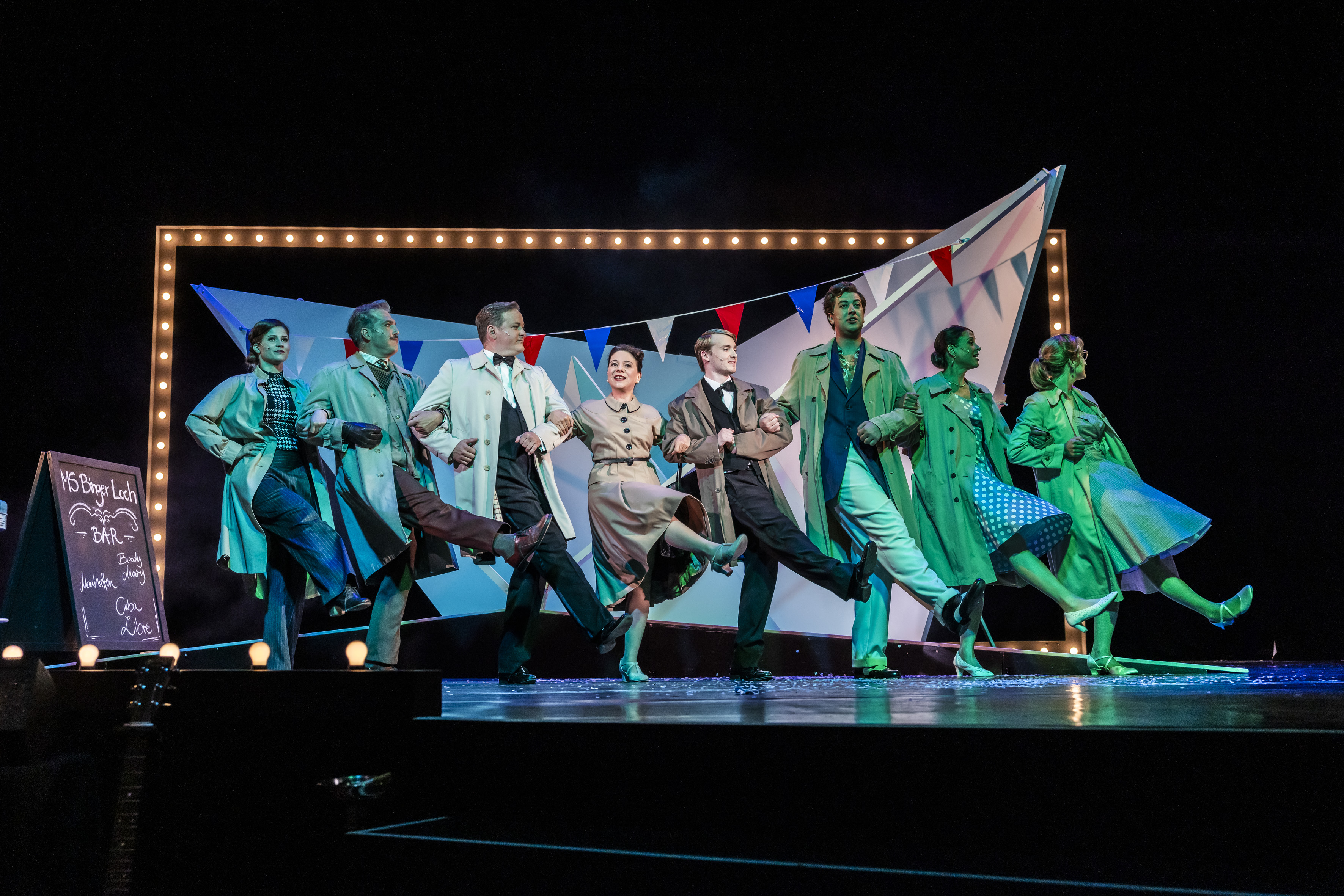 Ensemble des Theater Lüneburg bei einer Aufführung von "Petticoat und Minirock", tanzend in einer Reihe auf der Bühne.